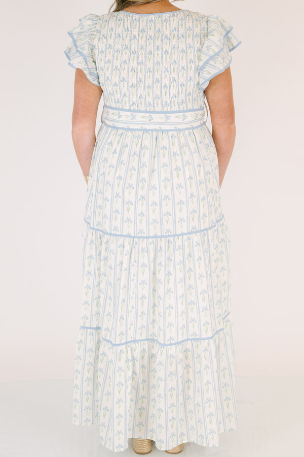 Chic Soul plus size clothing, white tiered dressed with a smocked texture on the chest flutter sleeves a bow that ties around the waist and a blue floral pattern throughout 