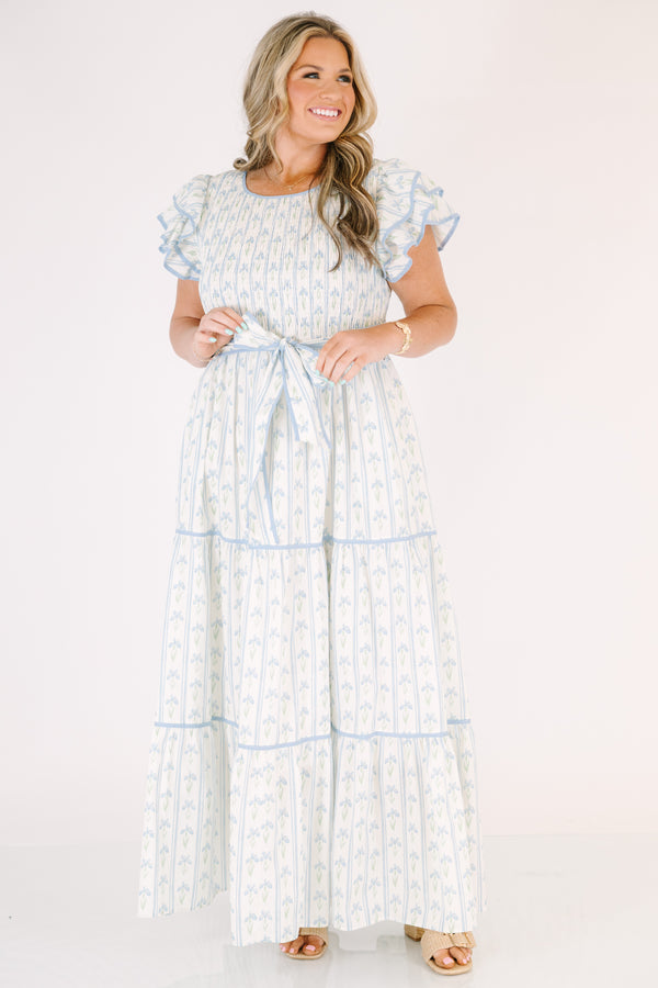 Chic Soul plus size clothing, white tiered dressed with a smocked texture on the chest flutter sleeves a bow that ties around the waist and a blue floral pattern throughout 