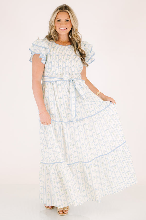 Chic Soul plus size clothing, white tiered dressed with a smocked texture on the chest flutter sleeves a bow that ties around the waist and a blue floral pattern throughout 