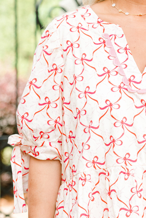 Plus Size white v-neck babydoll top with a pink bow print, ric rac trim, and tie-detail sleeves.