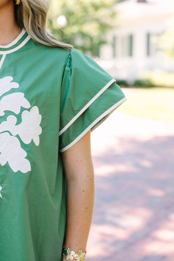 Plus size sage green top with white floral appliqué, ruffle sleeves, and a flowy silhouette.