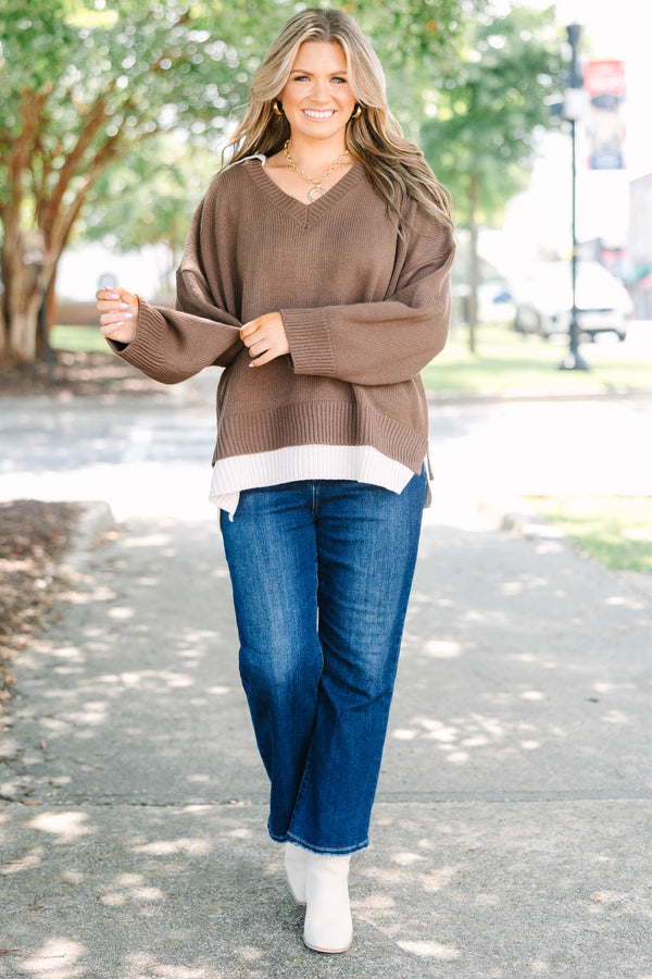 Plus size brown V-neck Sweater with a flowy fit and ribbed hem over blue jeans.