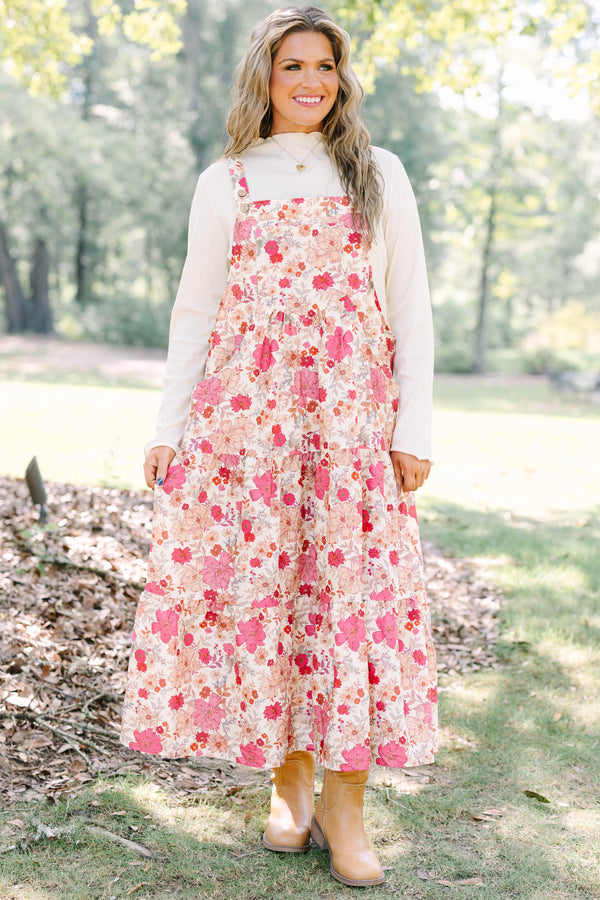Plus Size pink floral tiered midi dress with overall straps over a white long-sleeve top.