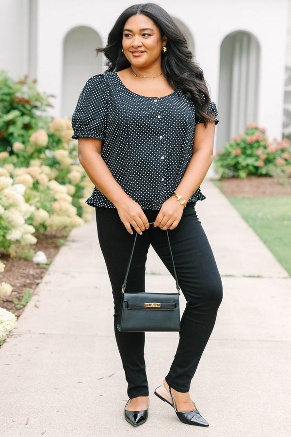 Short-sleeve black and white polka-dot blouse featuring a scoop neckline, front button closure, and a playful ruffled hem