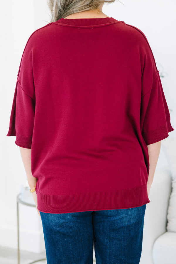 Plus size woman in a garnet red, oversized knit sweater with a flowy fit and short dolman sleeves.