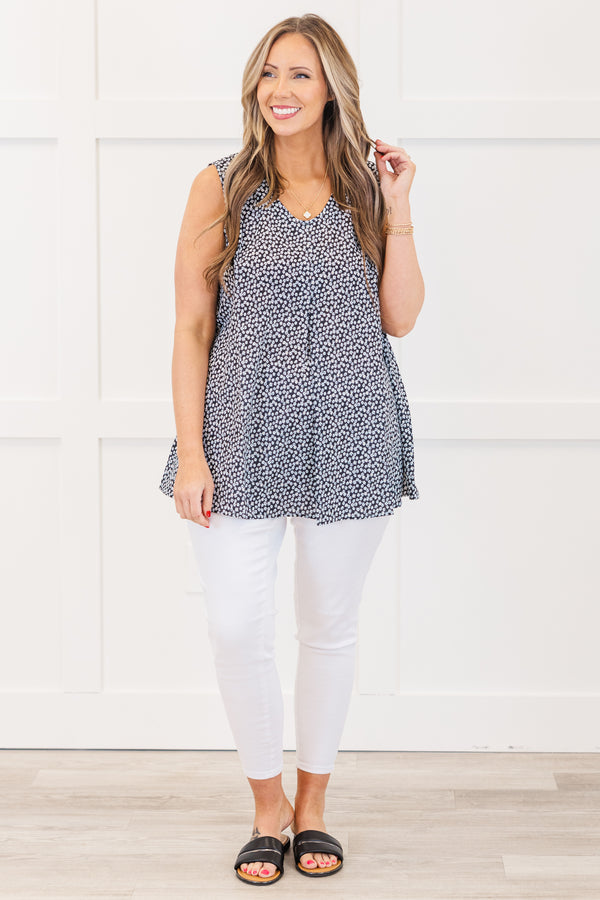 Plus Size black sleeveless top with a white floral pattern, V-neckline, and flowy pleated fit.