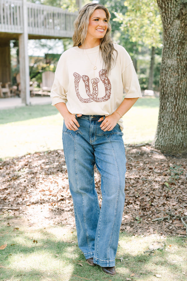 Plus Size cream short sleeve sweater with a brown horseshoe graphic and blue denim jeans.