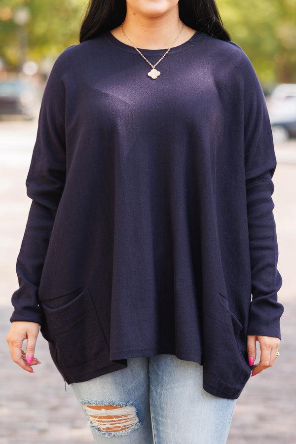 A woman smiles wearing a long-sleeved navy blue tunic with front pockets and light-wash jeans.