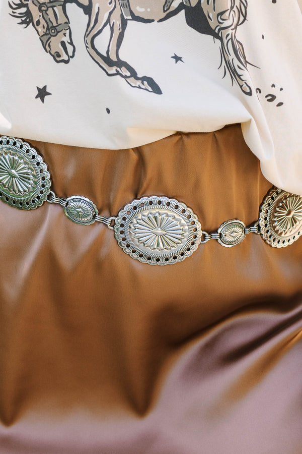 Plus Size silver concho chain belt with intricate sunburst engravings over a brown satin skirt.