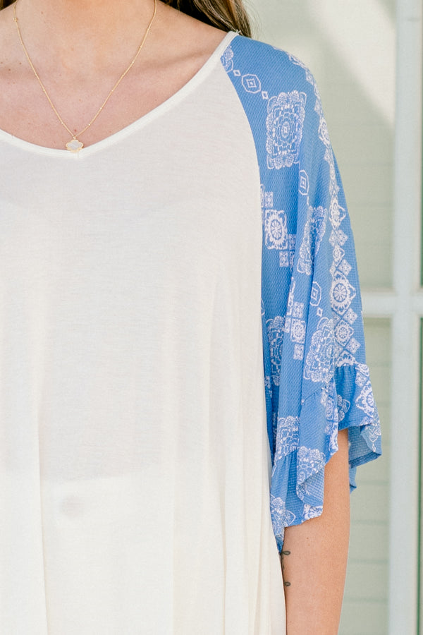 Plus Size white bodice top with blue abstract print raglan sleeves and a scoop neckline.