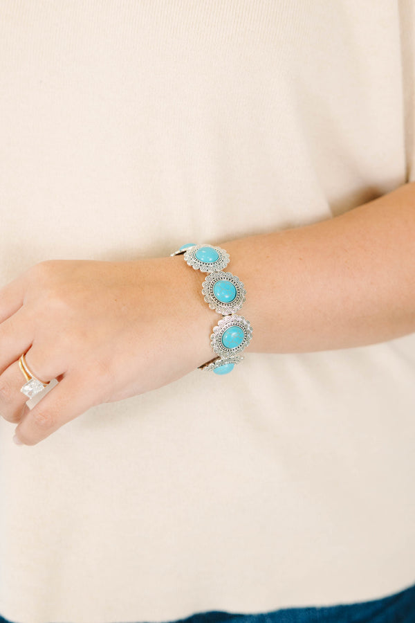 Silver stretch bracelet with round turquoise stones in ornate floral settings on a model's wrist.
