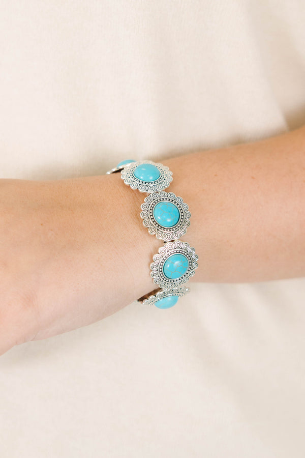 Silver stretch bracelet with round turquoise stones in ornate floral settings on a model's wrist.