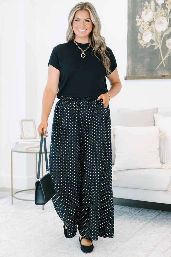 Plus size black wide-leg pants with white polka dots featuring a flowy fit and smocked waist.