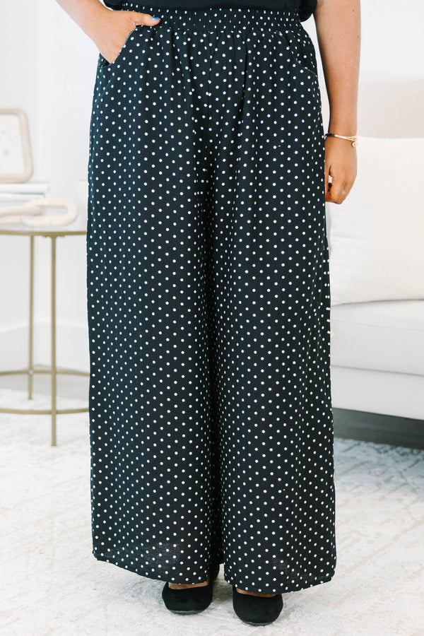 Plus size black wide-leg pants with white polka dots featuring a flowy fit and smocked waist.