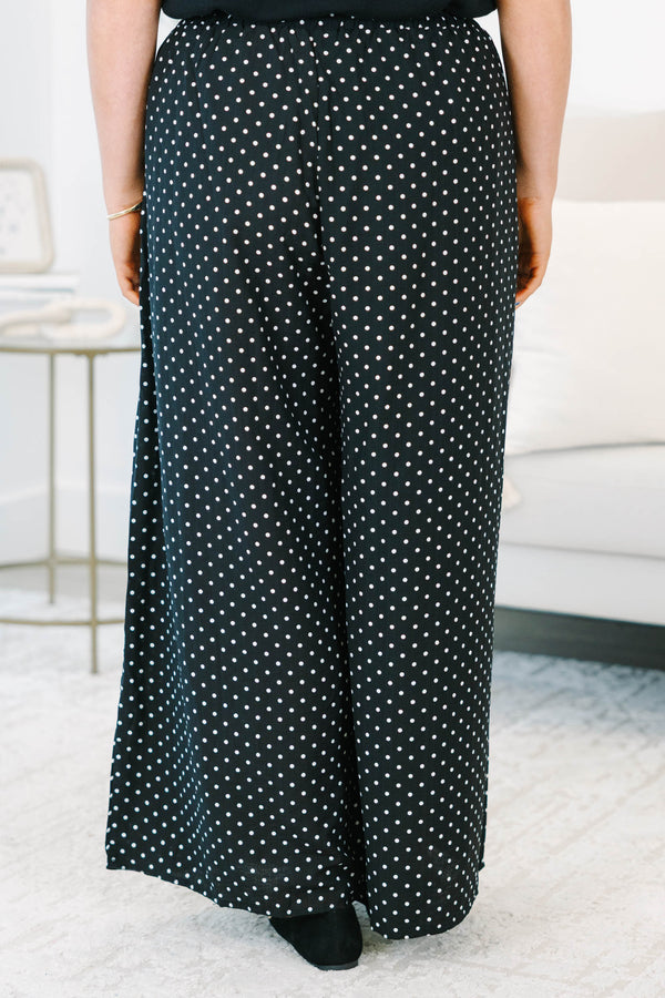 Plus size black wide-leg pants with white polka dots featuring a flowy fit and smocked waist.