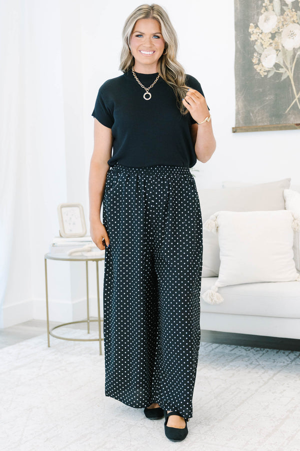 Plus size black wide-leg pants with white polka dots featuring a flowy fit and smocked waist.