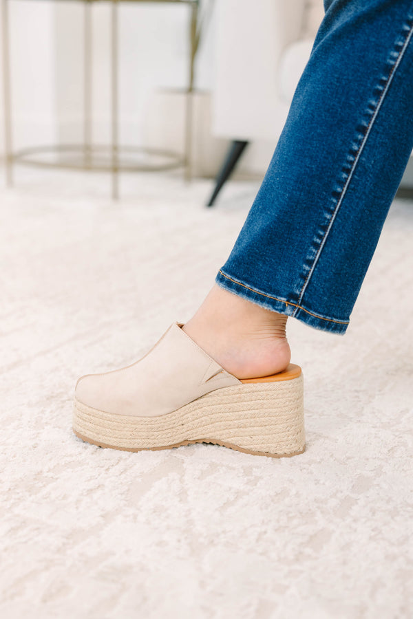 A person wearing sand-colored platform wedge mules with a woven jute sole