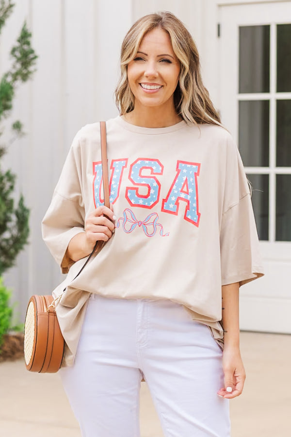 Plus Size light mocha oversized boyfriend tee with a USA star graphic and white pants.