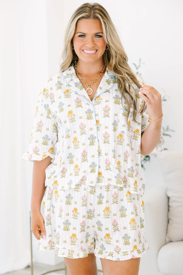 Plus Size white floral pajama set with short sleeves, button-down top, and matching ruffled shorts.