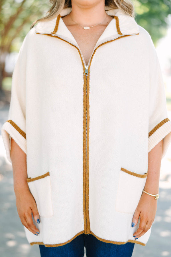 Plus size cream zip-up poncho sweater with brown trim, front pockets, and a flowy, relaxed fit.