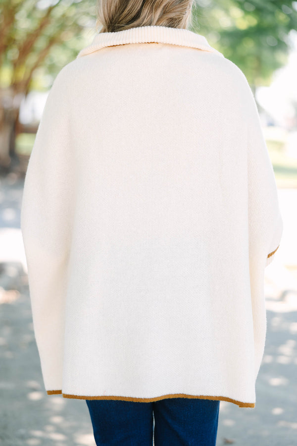 Plus size cream zip-up poncho sweater with brown trim, front pockets, and a flowy, relaxed fit.