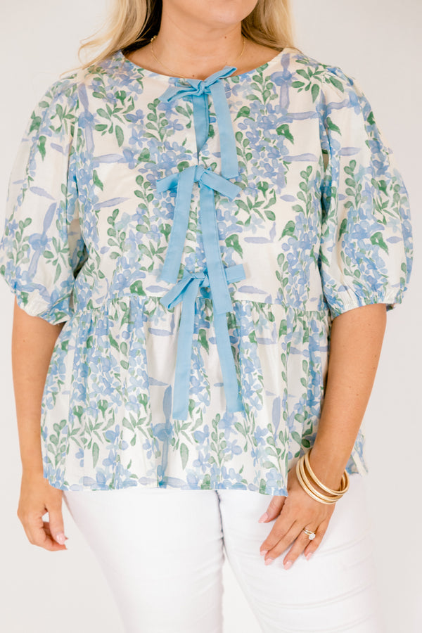 Chic Soul plus size clothing, white puff short sleeve babydoll top with light blue and green floral pattern and three blue bow ties down the middle of the top and cinching at the end of the sleeves