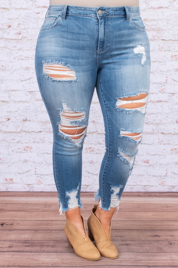 Plus Size medium wash skinny jeans with heavy distressing, ripped knees, and frayed hems.